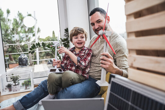 Father and son playing with wind turbine models sitting at home