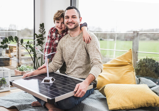 Smiling man with wind turbine and solar panel model by son at home