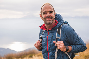 Smiling mature man with backpack standing under sky