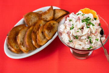 Crab salad in glass bowl, fried toast on plate on red table-cloth.