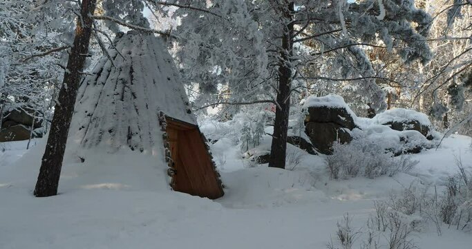 The traditional Siberian dwelling of the plague stands covered with snow in the winter forest. Hand held, the camera is moving.