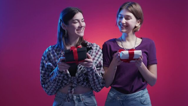 Festive present. Happy female friends. Neon light people. Excited two women holding gift boxes posing blue purple background.