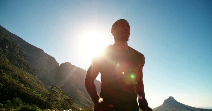 Wide angle slow motion video of an athlete running along a road with a bright sun and intense sky behind