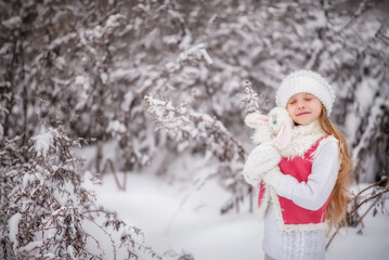 Beautiful little girl with long hair. Little girl in the winter forest. girl in a hat. Girl in a Zara sheepskin coat. A little girl hugs a toy hare. Winter. Snow. Tender baby. Baby girl portrait, Toy 