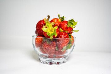 photo close up shot of a transparent bowl full of fresh and delicious strawberries on a white background
