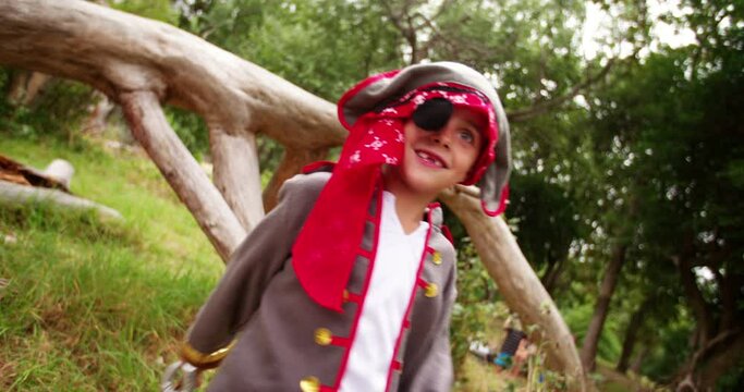 Smiling dressed up pirate boy with missing teeth attacking and fighting with his saber on a treasure hunt in nature.