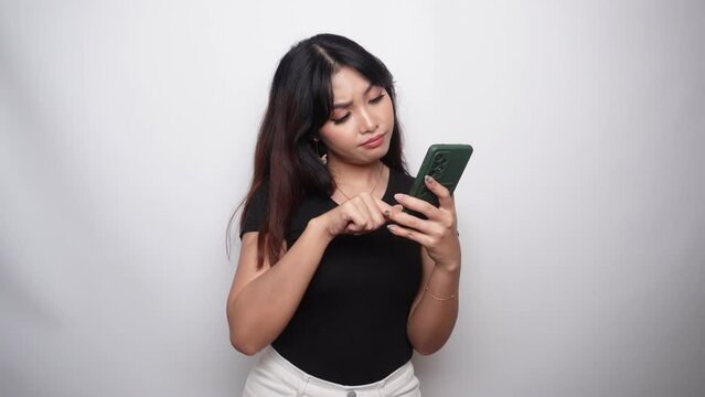A thoughtful young woman in black shirt and holding her chin with phone on hand isolated by white background