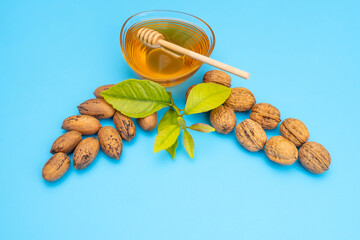 Blue festive background of pecan walnuts and a transparent bowl with honey with a wooden stick and green leaves