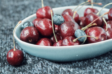Bowl full of ripe red cherries on a dark blue knitted blanket.