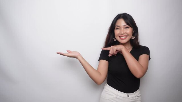 Excited Asian woman dressed in black shirt, pointing at the copy space beside her, isolated by white background