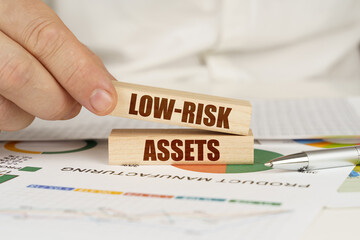 On the table are business charts and diagrams in the hands of a wooden block with the inscription - Low-risk assets