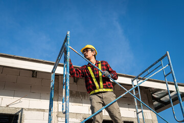 Naklejka premium Construction worker wearing safety harness and safety line working on scaffolding at new house under construction.