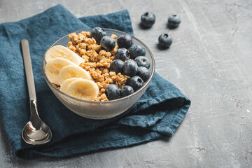 Granola cereal oatmeal with blueberries and banana fruits in a bowl on a grey background