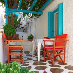 A tranquil house yard covered by green foliage with colorful orange chairs. Travel to Milos island, Greece.