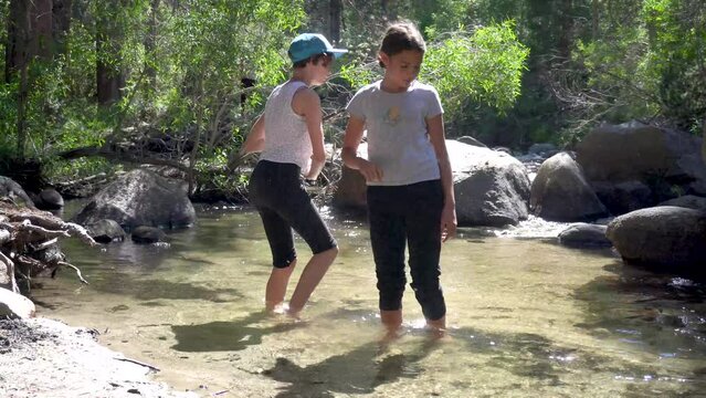 Sisters fight off mosquitos while they wade in a creek