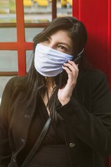 Beautiful hispanic woman talk on the phone with mask for new normal