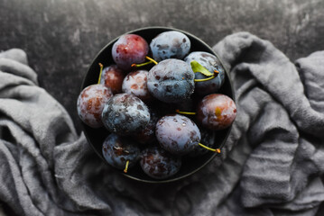 Top view of bowl of fresh picked plums on black background.
