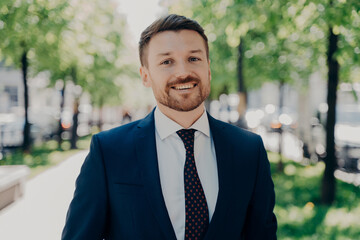 Close portrait of smiling handsome young bearded businessman outdoors