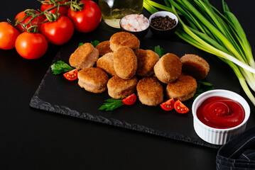 fried chicken nuggets on a black plate, ketchup in a saucepan, v