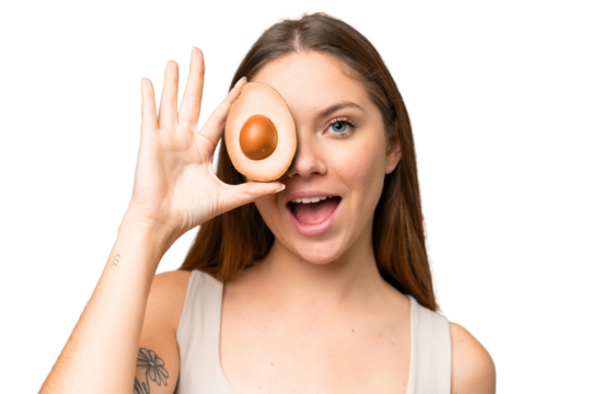 Young blonde woman over isolated chroma key background holding an avocado while smiling. Close up portrait
