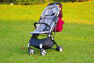 lawn baby stroller, modern black baby stroller on grass, red bag, gray fabric stroller