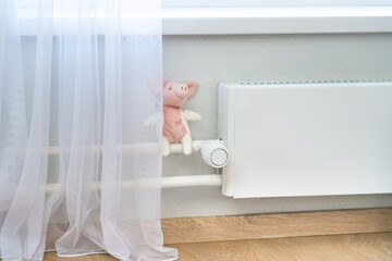 White heating radiator with thermostat regulator and soft toy in childrens room at home. Concept of central heating system. Heat saving.