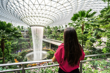 Young female tourist looking at the indoor waterfall in Changi Airport, Singapore - obrazy, fototapety, plakaty