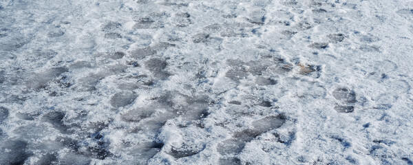 People footprints on slippery icy footpath in winter or spring season. Pedestrian walks safety problem.