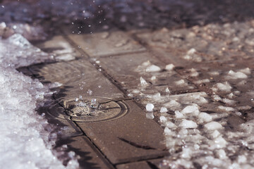 Drop of melting water fallen in puddle on sidewalk in springtime. Snowbroth covered urban pavement...