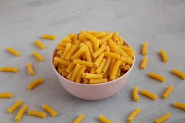 Dry Rigatoni Pasta in a Pink Bowl on a gray background, side view.