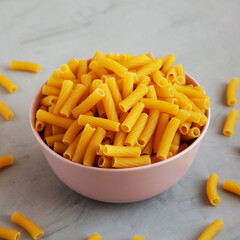 Dry Rigatoni Pasta in a Pink Bowl on a gray background, low angle view.