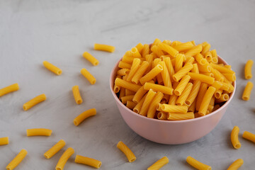 Dry Rigatoni Pasta in a Pink Bowl on a gray background, side view.