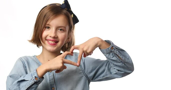 Smiling little girl make heart sign with hands in casual denim dress isolated on white background, studio, makes love icon, gesture with fingers Heart symbol, love concept.