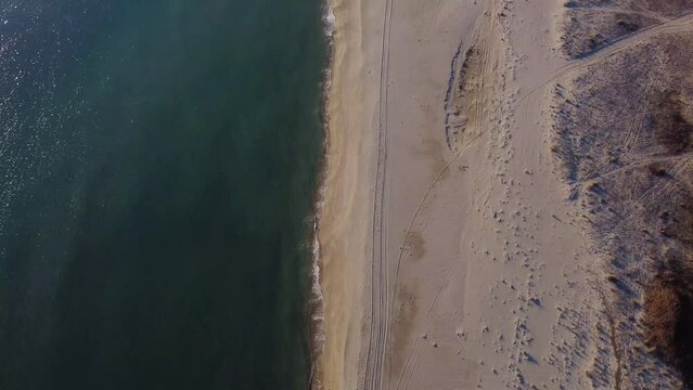 Aerial top down following tire tracks on sandy beach.