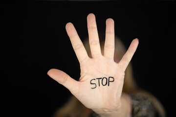 Woman showing hand stop sign with word STOP written to campaign against gender violence and pain. Hand raised to dissuade for self harm awareness, stop abusing, bullying, mental health. Copy space. - obrazy, fototapety, plakaty