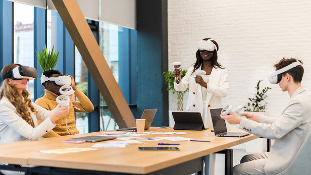Business conference in VR in an office. Multiracial group of people using VR glasses and controllers, papers and gadgets on the table