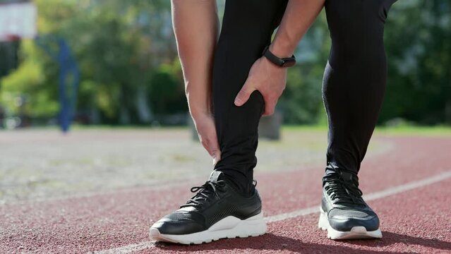 Close up; injured leg of a male athlete at the city stadium. Man massaging stretching, trauma injury while jogging outdoors. Fitness male sprain severe pain stretch pull. Leg muscle cramp calf sport