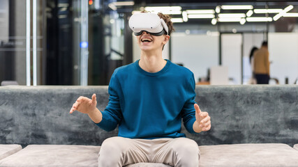 An excited young man exploring virtual reality using VR glasses in an office