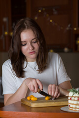 Young woman cuts fresh kumquat citrus on a wooden board on the kitchen table. The concept of healthy food, culinary arts, vegetarianism, diet. Freshly squeezed orange juice. Alkaline diet.