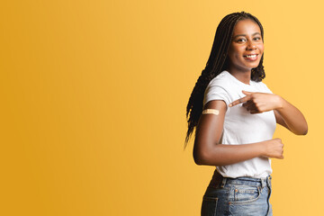 Cheerful african-american woman with medical patch aid on the forearm after vaccination pointing...