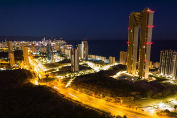 Benidorm coastline at night with tall buildings and mountains in the background. Aerial shot by drone