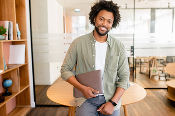 Smart and ambitious african-american male office employee posing with laptop indoor, friendly black...