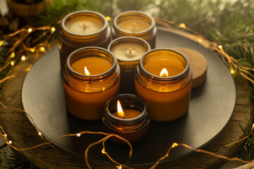 Soy candles burn in glass jars. Comfort at home. Candle in a brown jar. Scent and light. Scented handmade candle. Aroma therapy. Christmas tree and winter mood. Cozy decor. Festive garland decoration