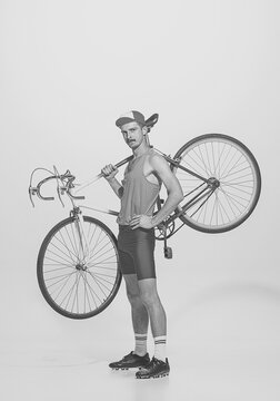 Black and white portrait of young man in sports uniform holding bike on shoulder, posing and looking at camera. Retro vintage sport, fashion, art