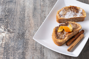 Traditional homemade Spanish torrijas decorated with cinnamon and orange peel on wooden table
