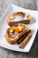 Traditional homemade Spanish torrijas decorated with cinnamon and orange peel on wooden table