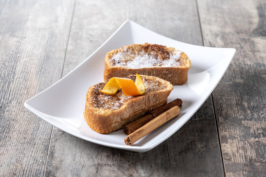 Traditional homemade Spanish torrijas decorated with cinnamon and orange peel on wooden table