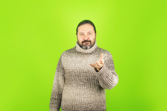 An adult man in a warm sweater on a plain green background. Template with a smiling man and an empty outstretched hand with a place for an object. - Powered by Adobe