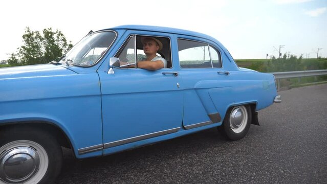 Young couple driving on country road in vintage automobile. Trip at the retro auto. Concept of summer vacation or holiday. Classic old car traveling on highway on summer day.  Slow motion Close up