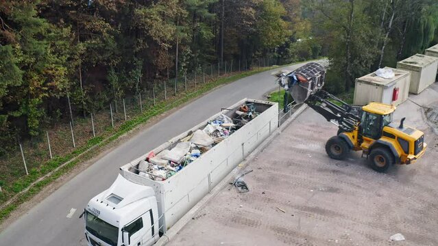 Skid steer loader loading a truck with waste material transferred for further sorting, treatment, and recycling, aerial view. Waste disposal and waste management concept.
